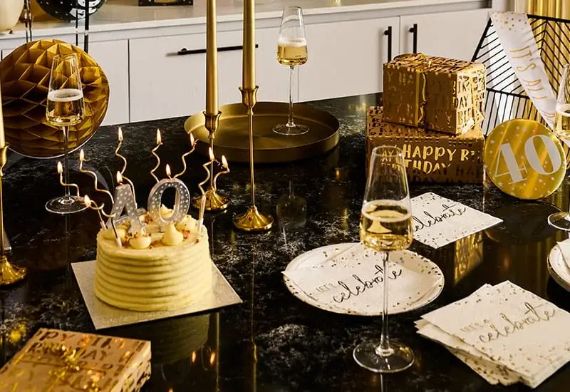 40th birthday celebration table with a birthday cake, number 40 candles, champagne glasses, gold gift boxes, and black-and-gold party decorations.